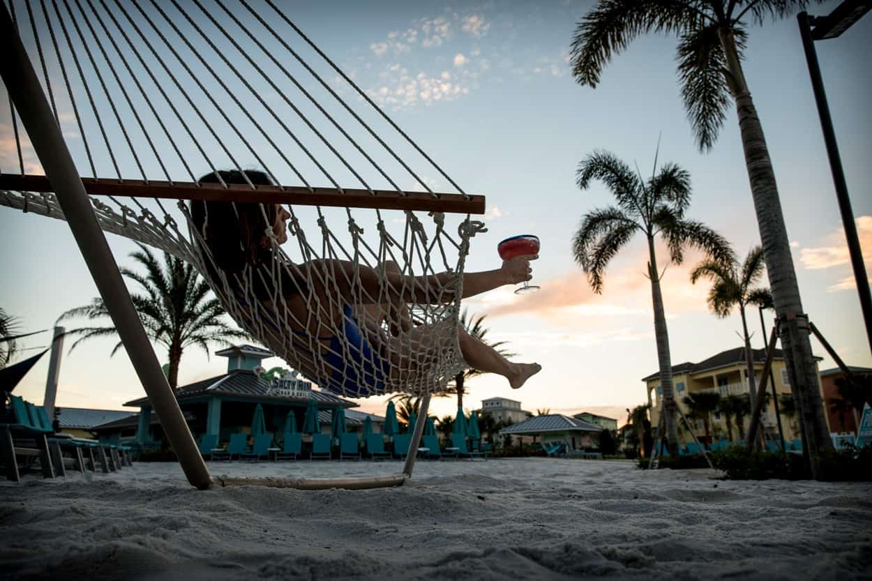 Woman lying in a hammock with a full margarita glass at Margaritaville Resort Orlando’s Fins Up Beach Club.