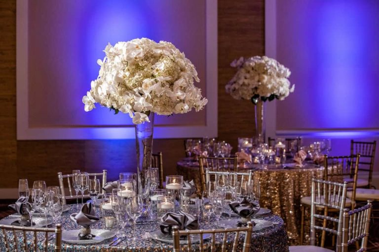 تم تزيين مساحة المناسبات في Margaritaville Resort Orlando لاستقبال حفل زفاف بترتيبات الأزهار على طاولات الطعام.