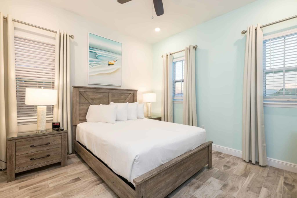 King bed in between two side tables and island-inspired wall art: 3 Bedroom Waters Edge Cottage
