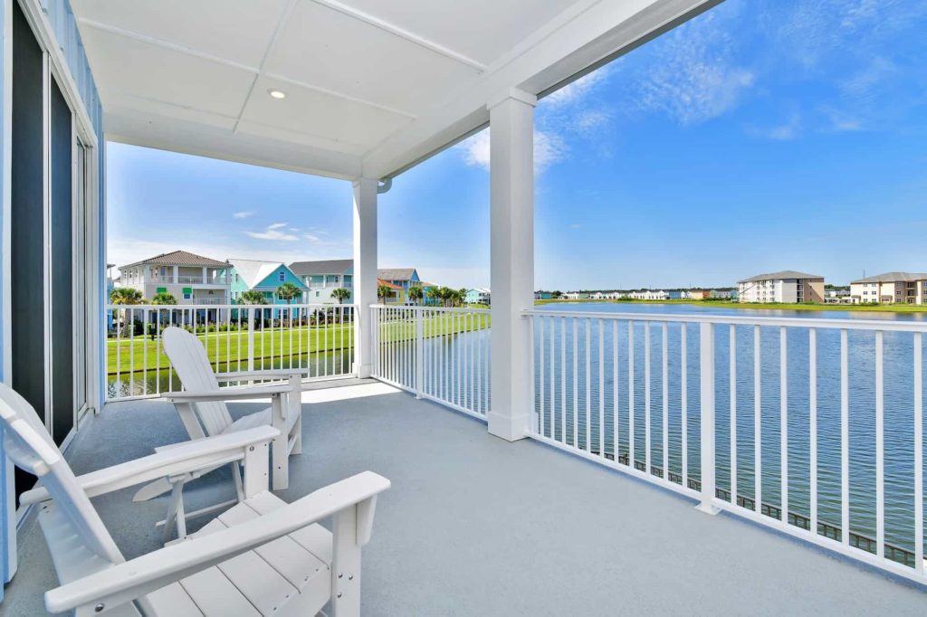 Covered balcony with two beach chairs overlooking the water: 3 Bedroom Water’s Edge Cottage with Pool