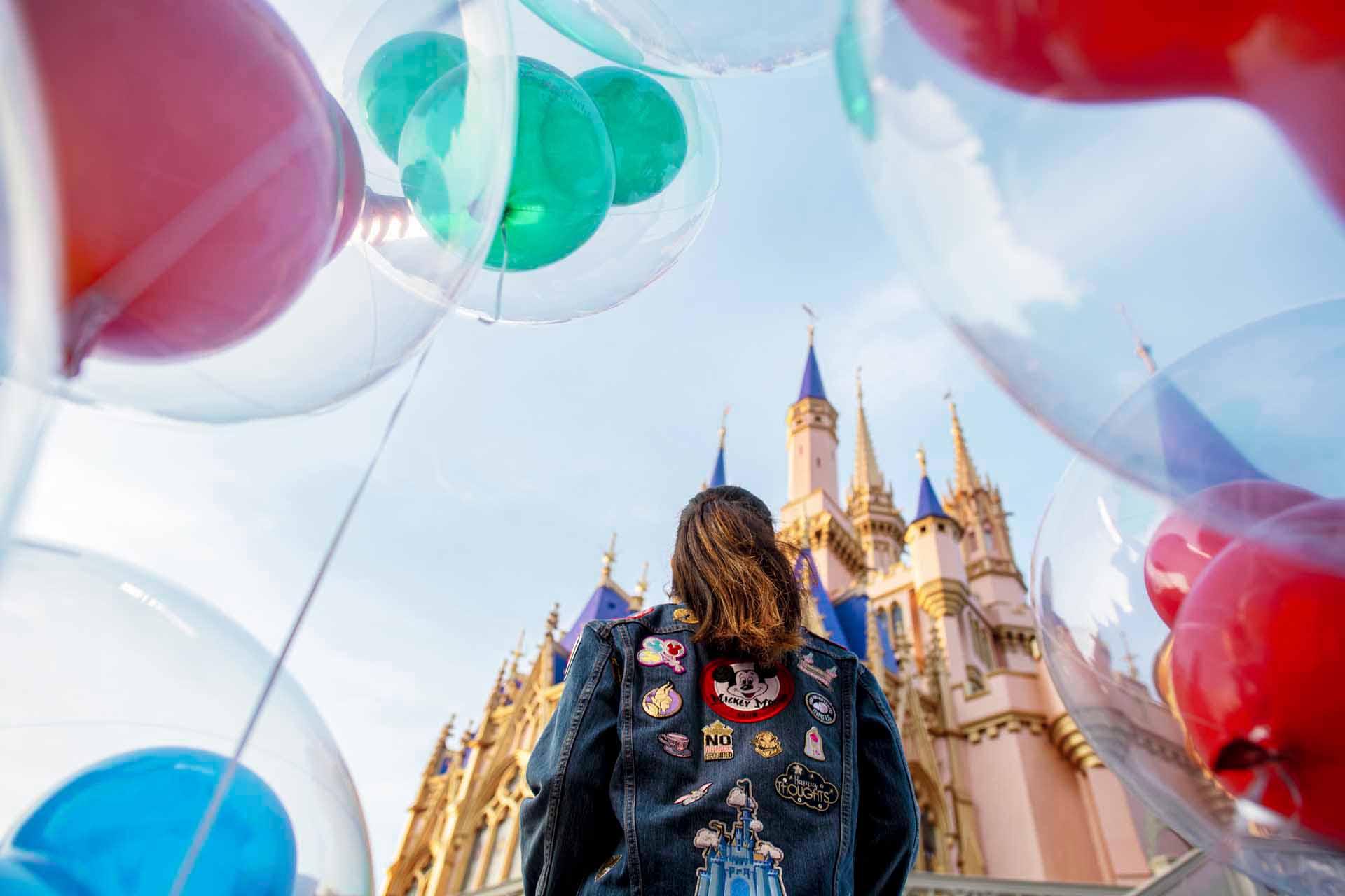 Girl standing in front of Cinderella's Castle at the Magic Kingdom, surrounded by balloons