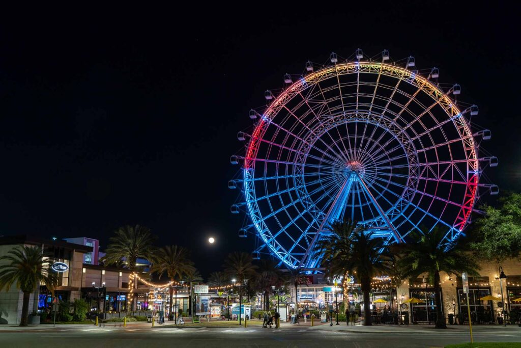View of the Wheel at ICON Park lit up at night as well as ICON Park restaurants and shops