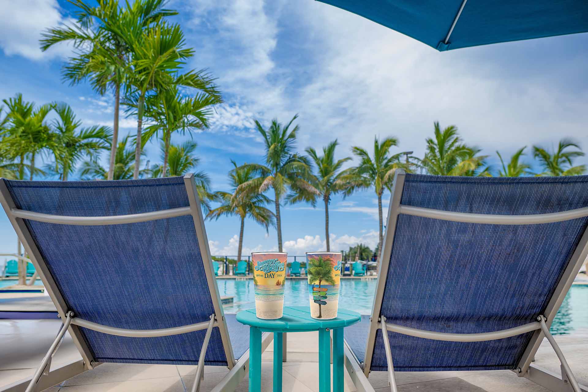 Jimmy Buffet Day glassware sitting on a table between 2 lounge chairs