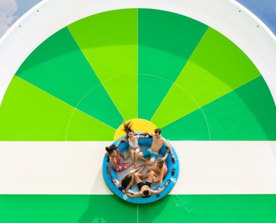Six people in a large tube ride up a ramp on an Island H2O Live water slide.