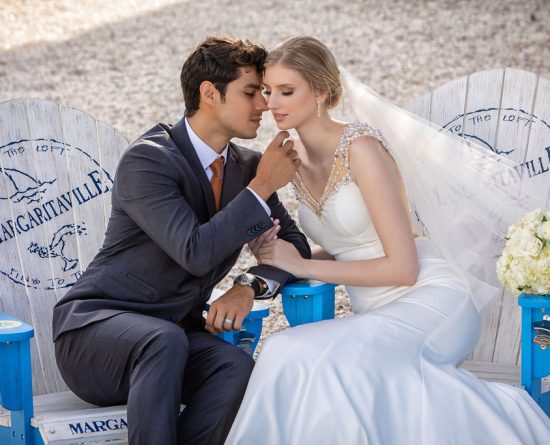 Braut und Bräutigam küssen beim Sitzen am Strand im Margaritaville Resort Orlando.