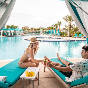 Young couple toasting with glasses of tropical drinks in a private poolside cabana.