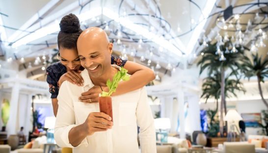 mro-lobby-couple-bloody-mary-rotated-e1611338944538 Husband and wife hugging and smiling in the Margaritaville Resort Orlando lobby.